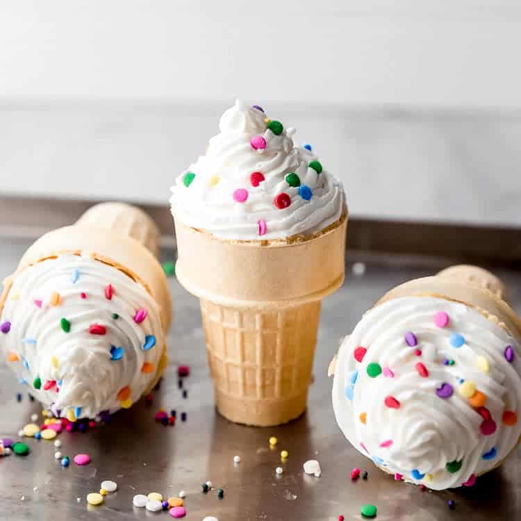 Three ice cream cones filled with cupcakes with frosting and sprinkles on a baking pan