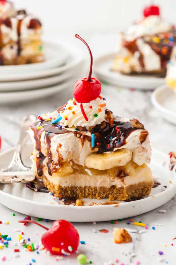Banana Split Cake on a white plate with a cherry on top