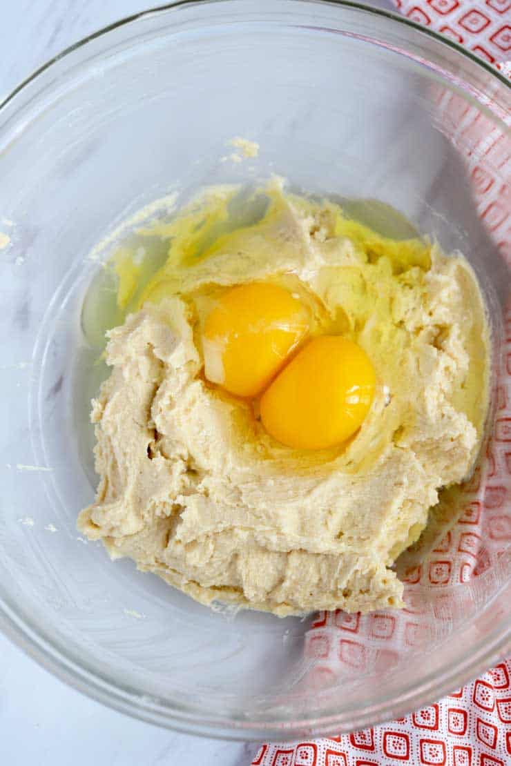 Creamed butter and sugars in a bowl topped with eggs.