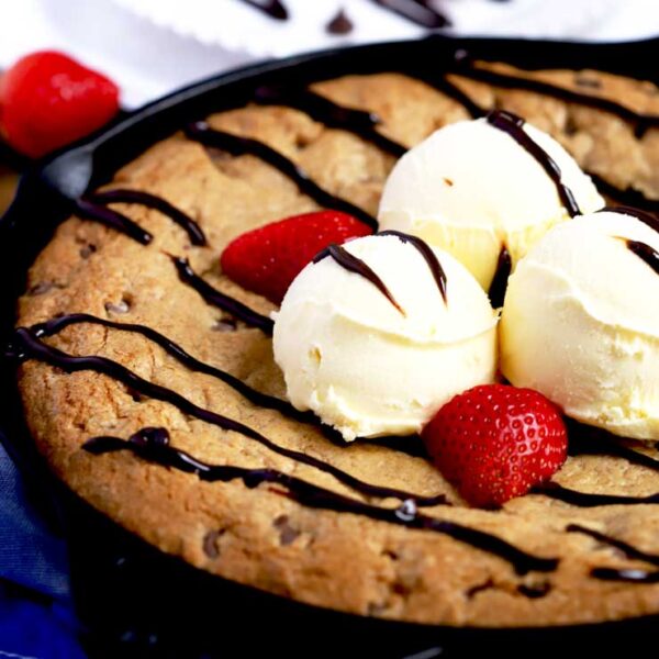 A chocolate chip cookie skillet with three scoops of vanilla ice cream on top, strawberries and hot fudge