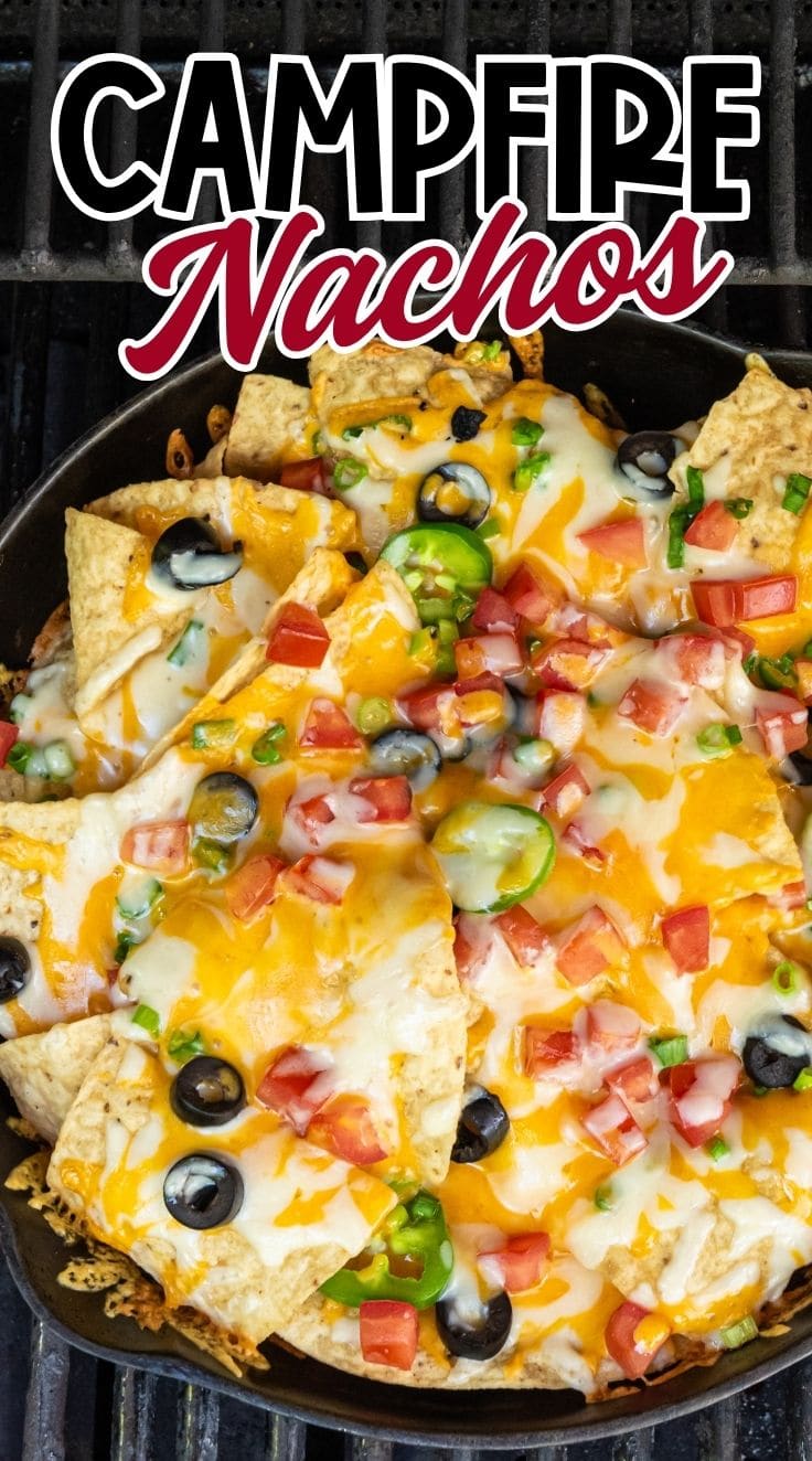 close up of campfire nachos in a skillet, topped with melted cheese, olives, tomatoes, and jalapenos.