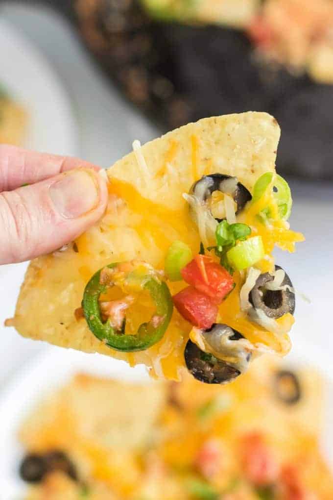 A tortilla chip with melted cheese peppers and olives