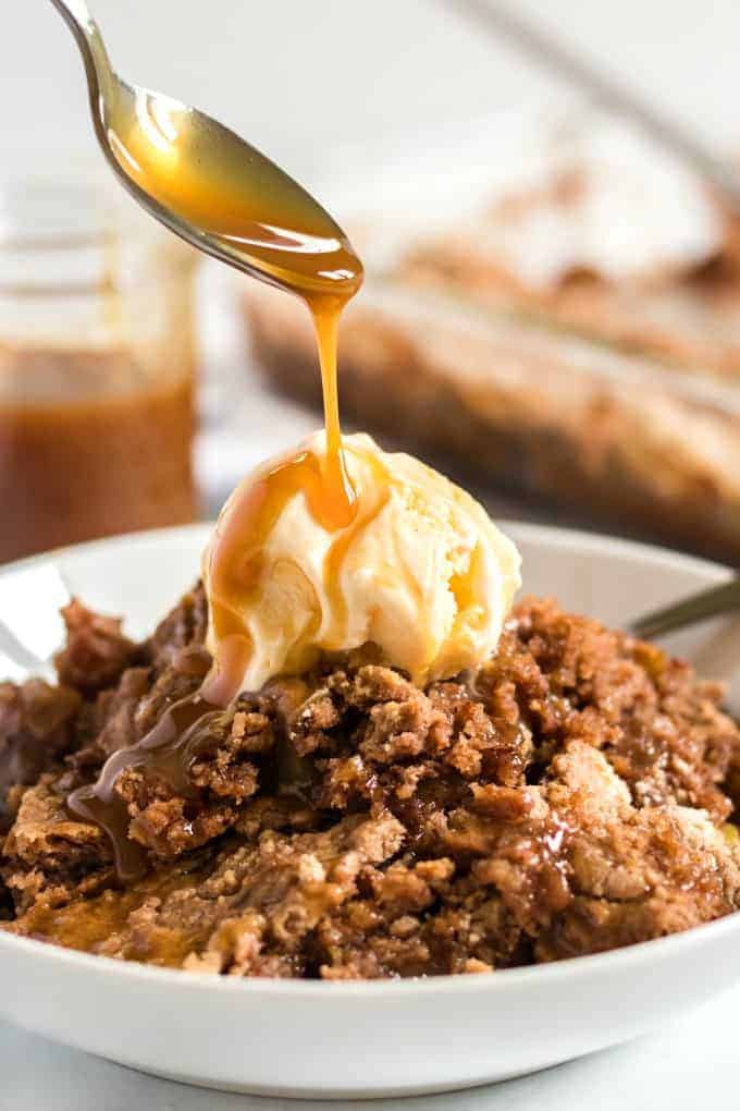 apple dump cake drizzled with caramel sauce in a white bowl