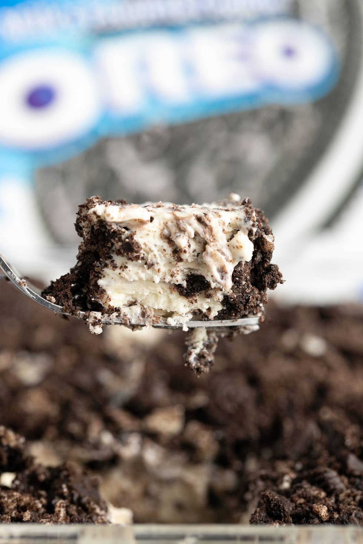 Close-up of a spoonful of Oreo cheesecake layered with crushed cookies and creamy filling.