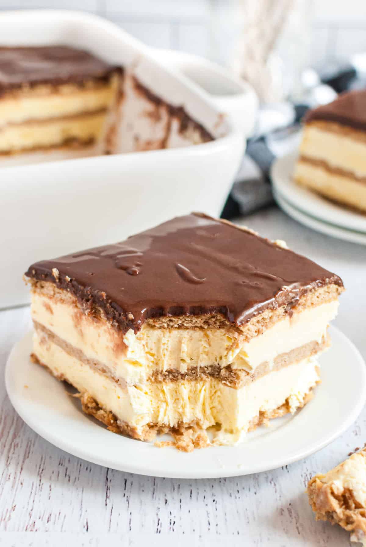 A piece of eclair cake on a white plate with a bite taken out 