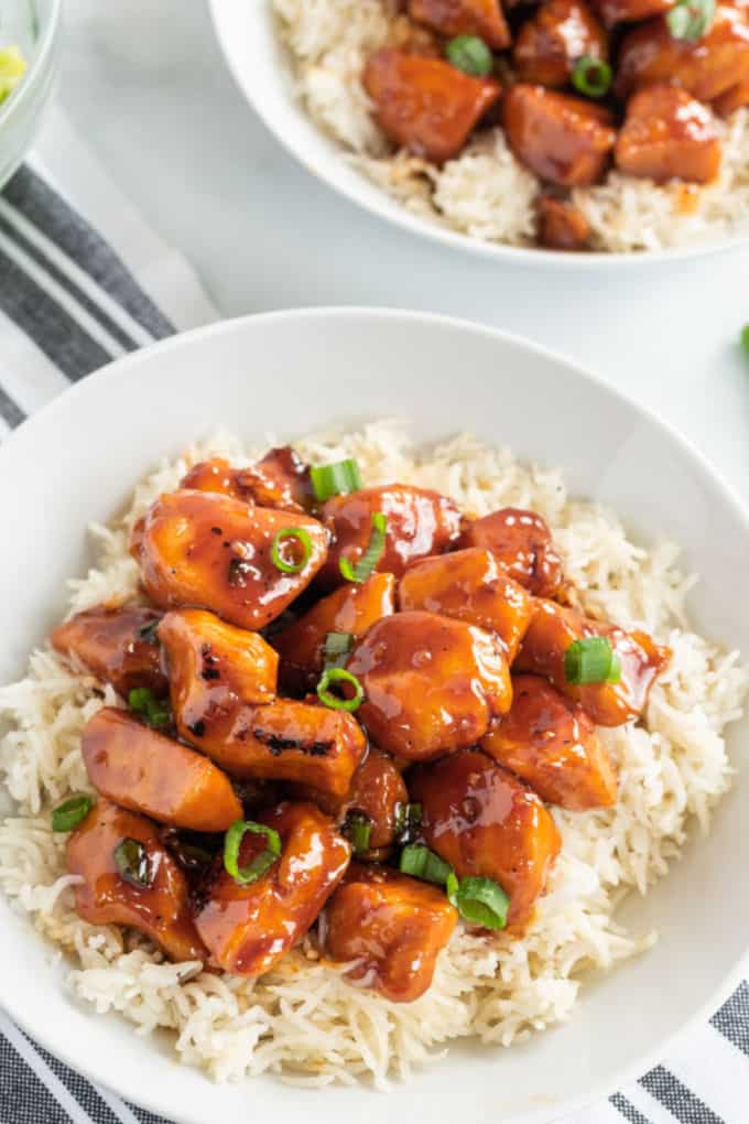 Chicken with bourbon sauce and scallions on rice in a white bowl