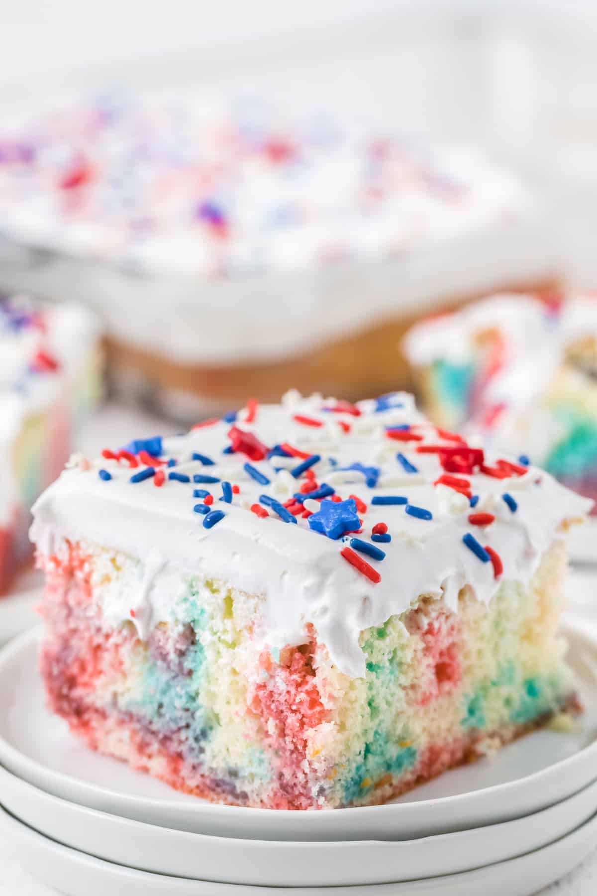 A close up of a piece of cake on a plate, with Sprinkles and red and blue streaks