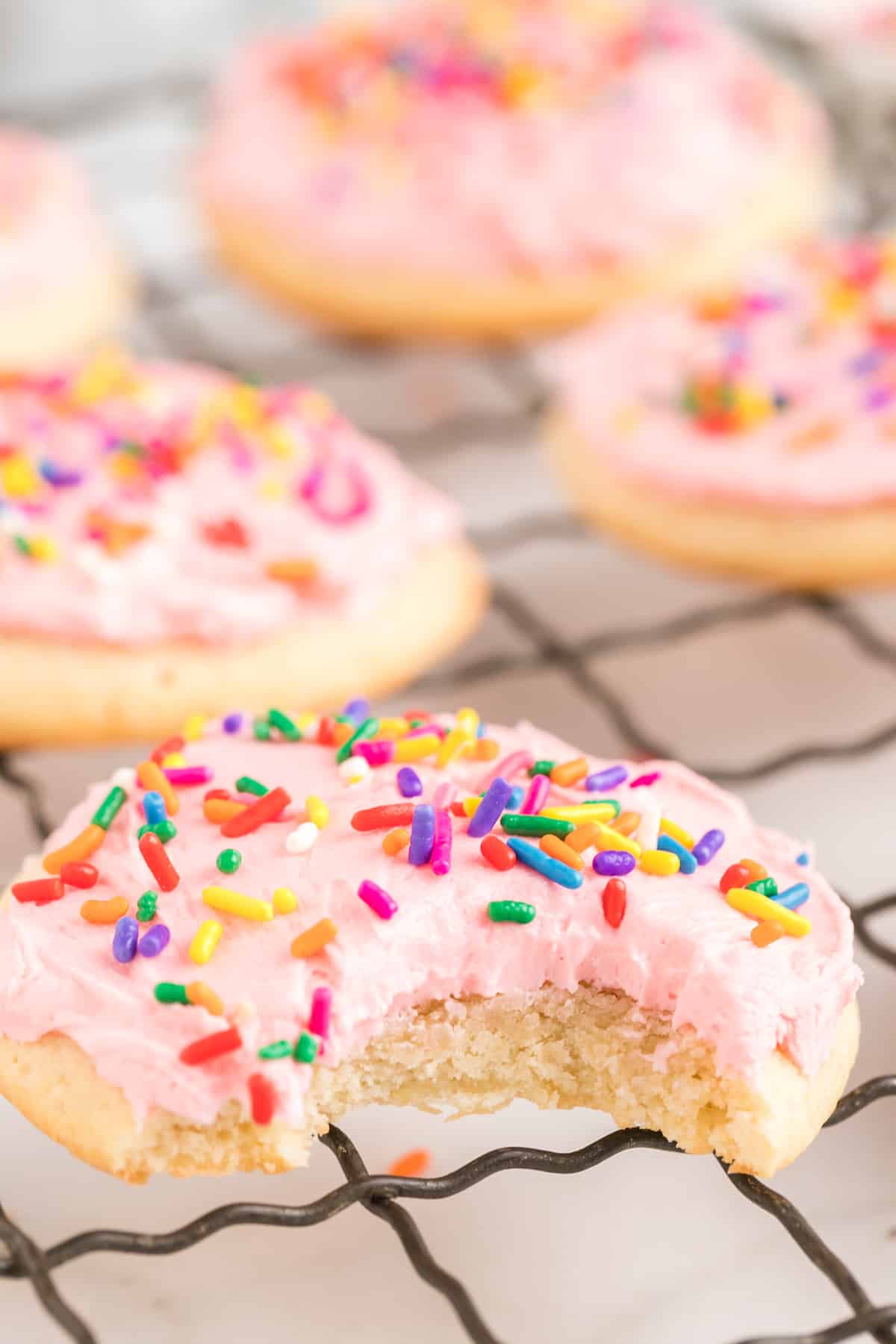A close up of a lofthouse cookie with pink frosting and sprinkles