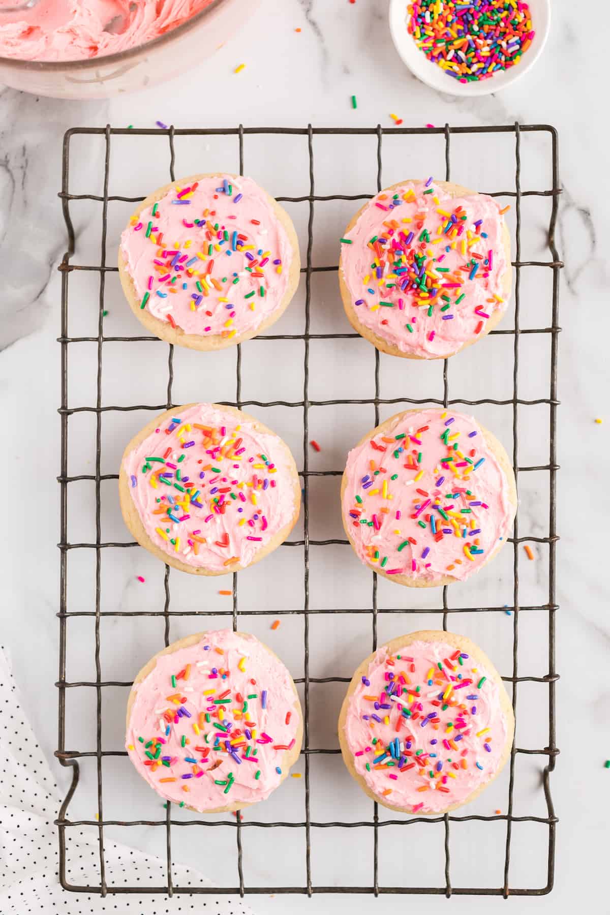 6 cookies with pink frosting and sprinkles on a wire cooling rack