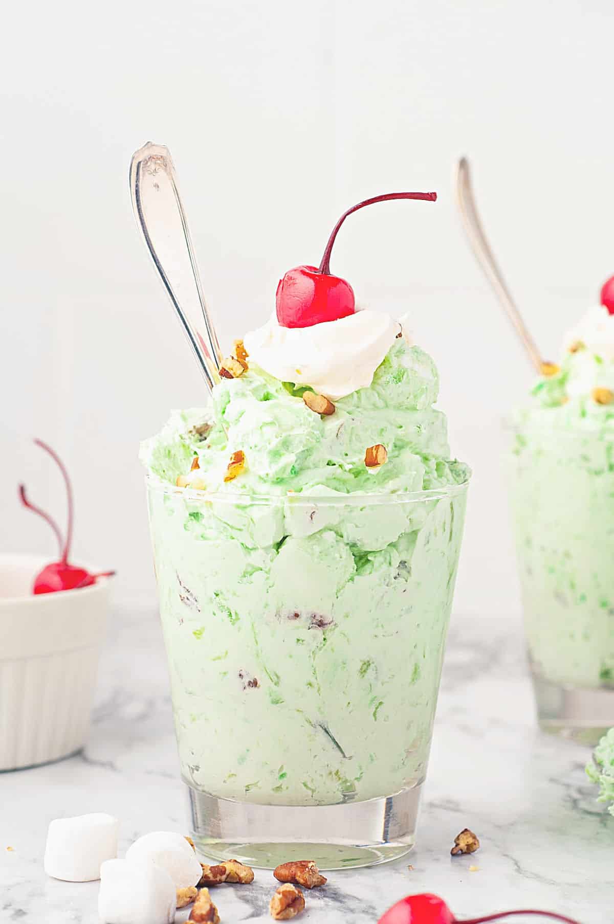 Watergate Salad in a glass with whipped topping and a cherry on top