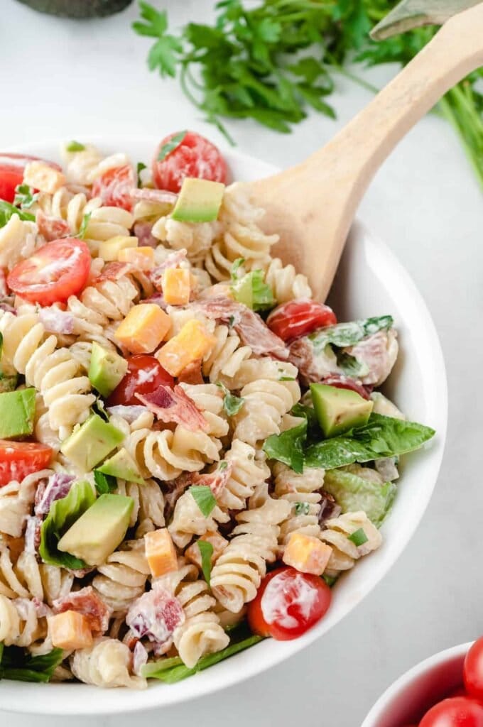 BLT Pasta Salad in a white bowl with a wooden spoon