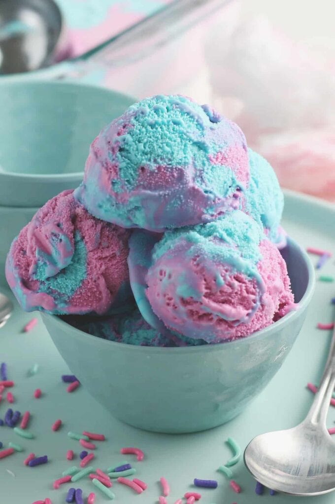 Pink and blue cotton candy ice cream in a blue bowl with sprinkles surrounding it