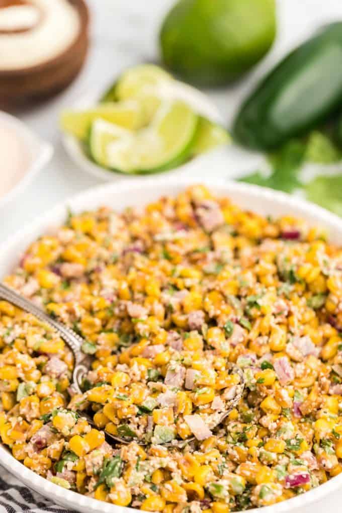 close up of corn salad in a white bowl with a spoon