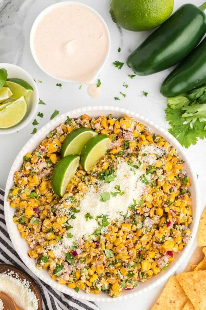 Mexican Corn Salad in a white dish with cheese and limes on top