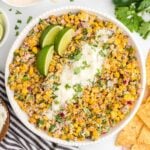 Mexican Corn salad in a white bowl with lime wedges and cheese on top