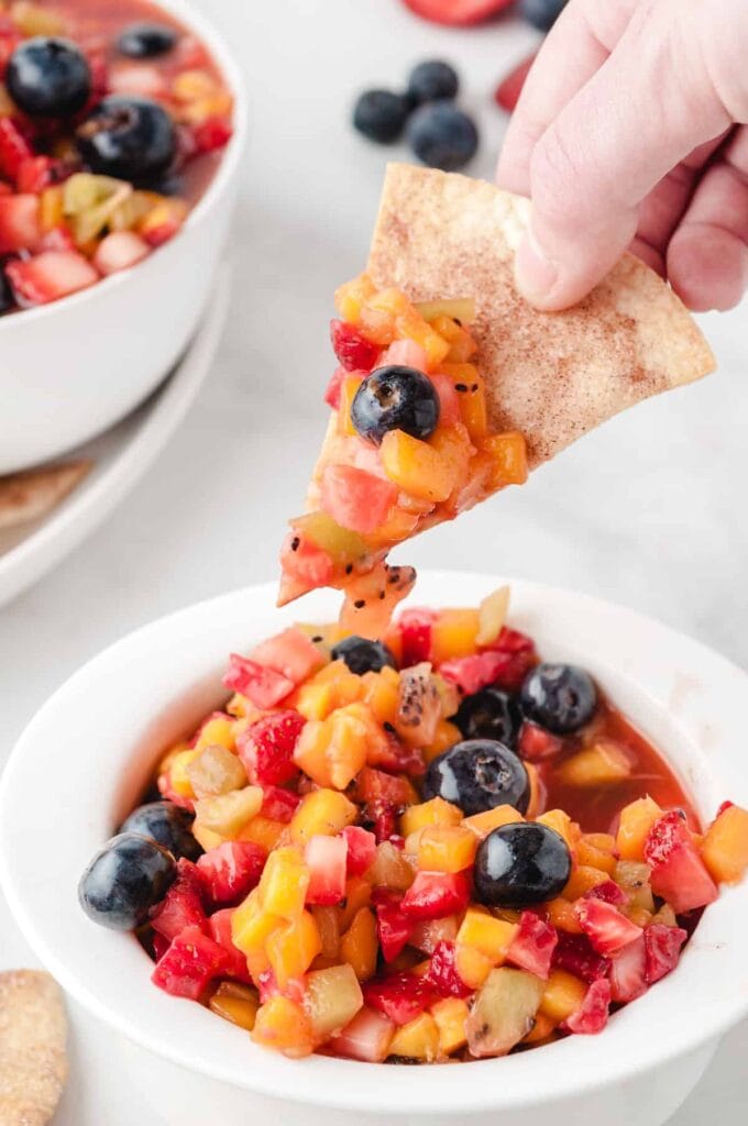 a cinnamon sugar chip being dipped in a bowl full of fruit