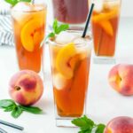 peach iced tea with a piece of peach floating in the glass and a peach next to it on the table