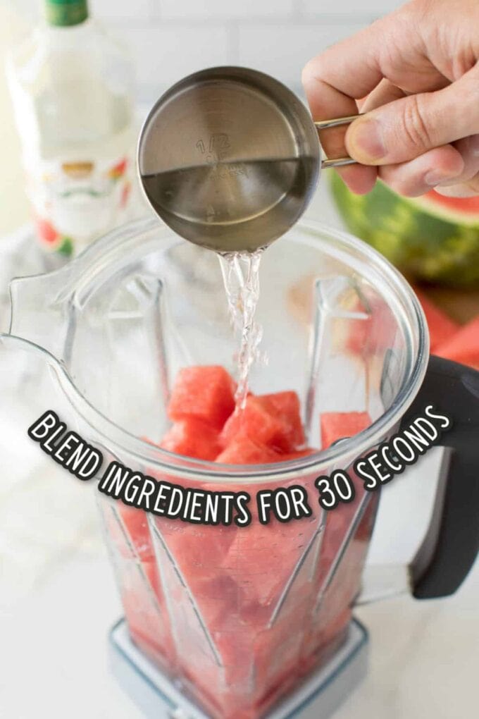 Pouring vodka in a blender with chunks of watermelon