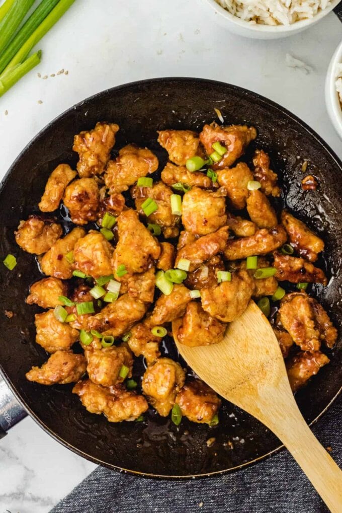 chicken in a black pan with a wooden spoon