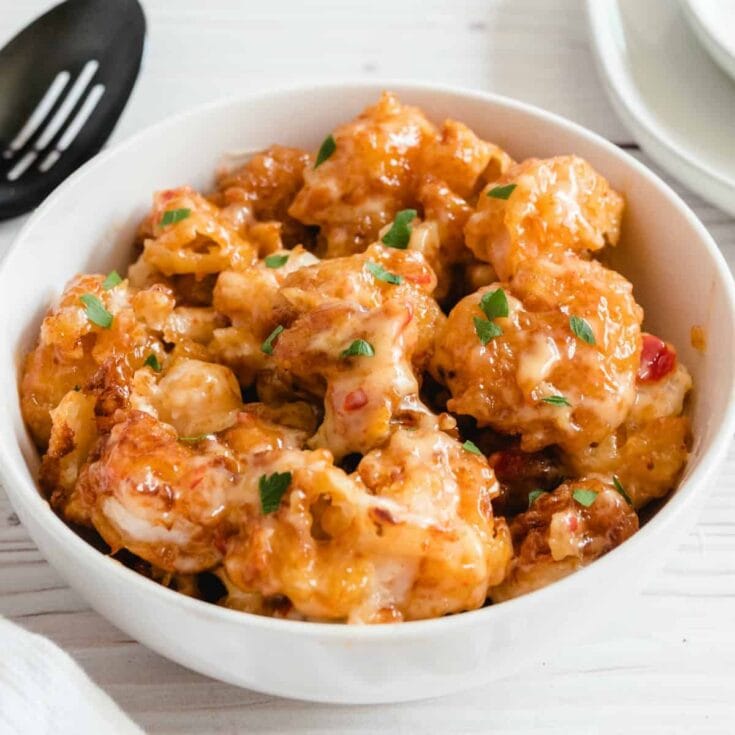 Bowl of crispy Bang Bang shrimp in glossy orange sauce with parsley and red peppers.