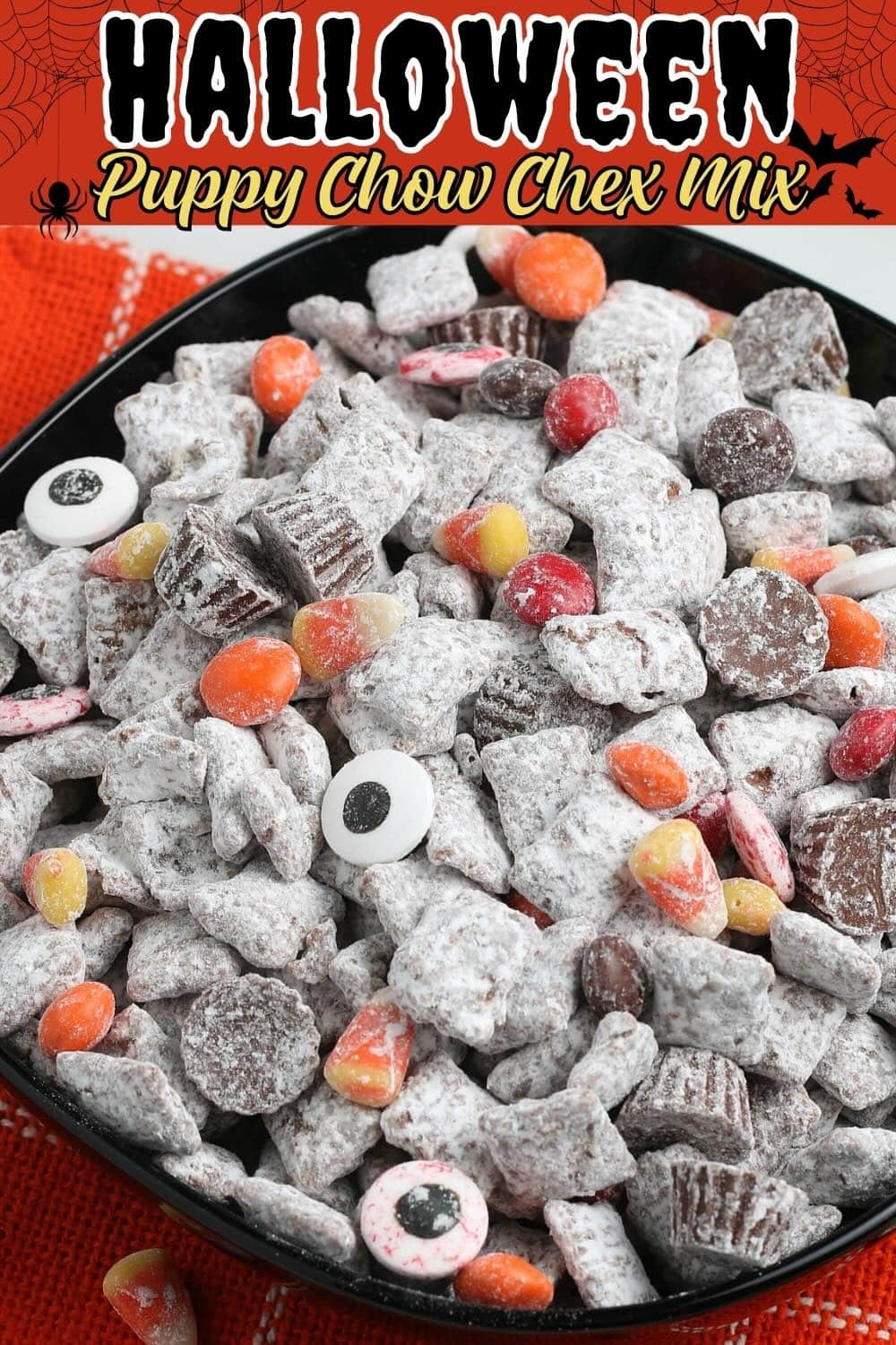 Halloween puppy chow Chex mix in a black bowl with candy eyeballs, candy corn, and peanut butter cups.