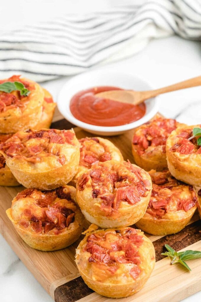 Pizza muffins stacked on top of each other with marina sauce dip in the background