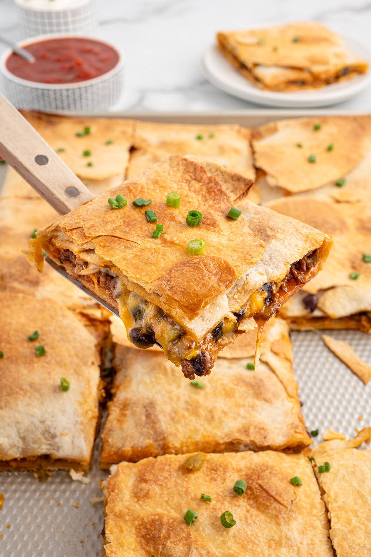 Beef sheet pan quesadillas with melted cheese and black beans, cut into squares and topped with green onions.