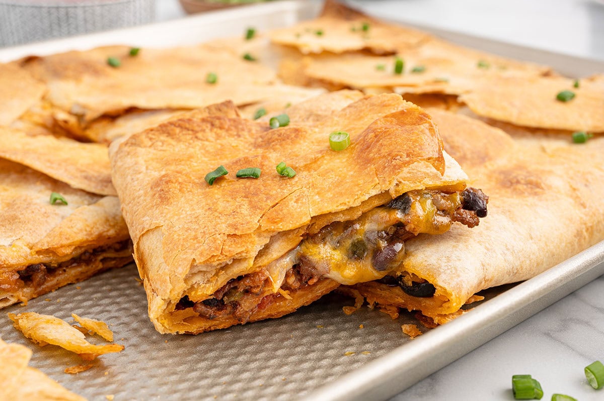 Crispy beef sheet pan quesadilla with melted cheese and black beans, topped with green onions on a baking sheet.