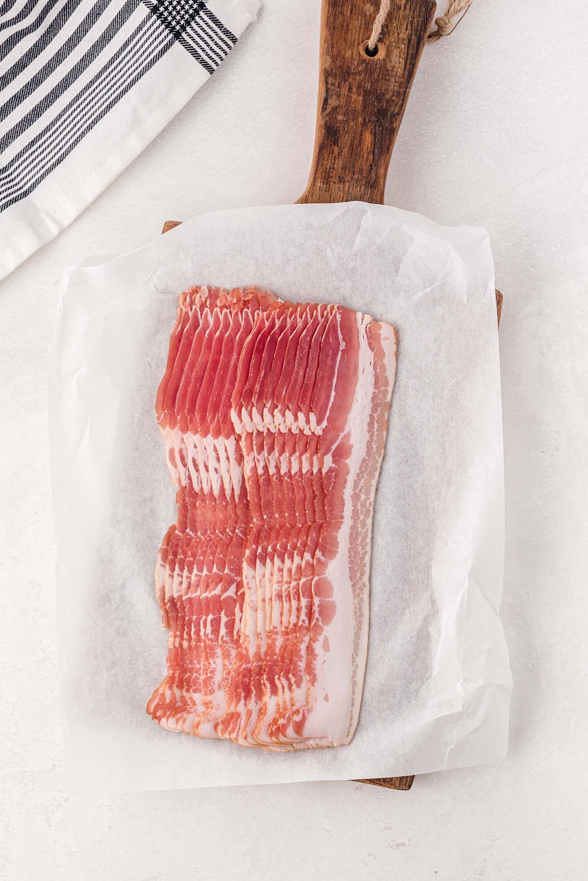 slices of raw bacon on top of wooden tray. 