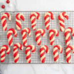 Rows of red and white candy cane-shaped cookies on a wire cooling rack, with ornaments nearby.