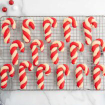 Rows of red and white candy cane-shaped cookies on a wire cooling rack, with ornaments nearby.
