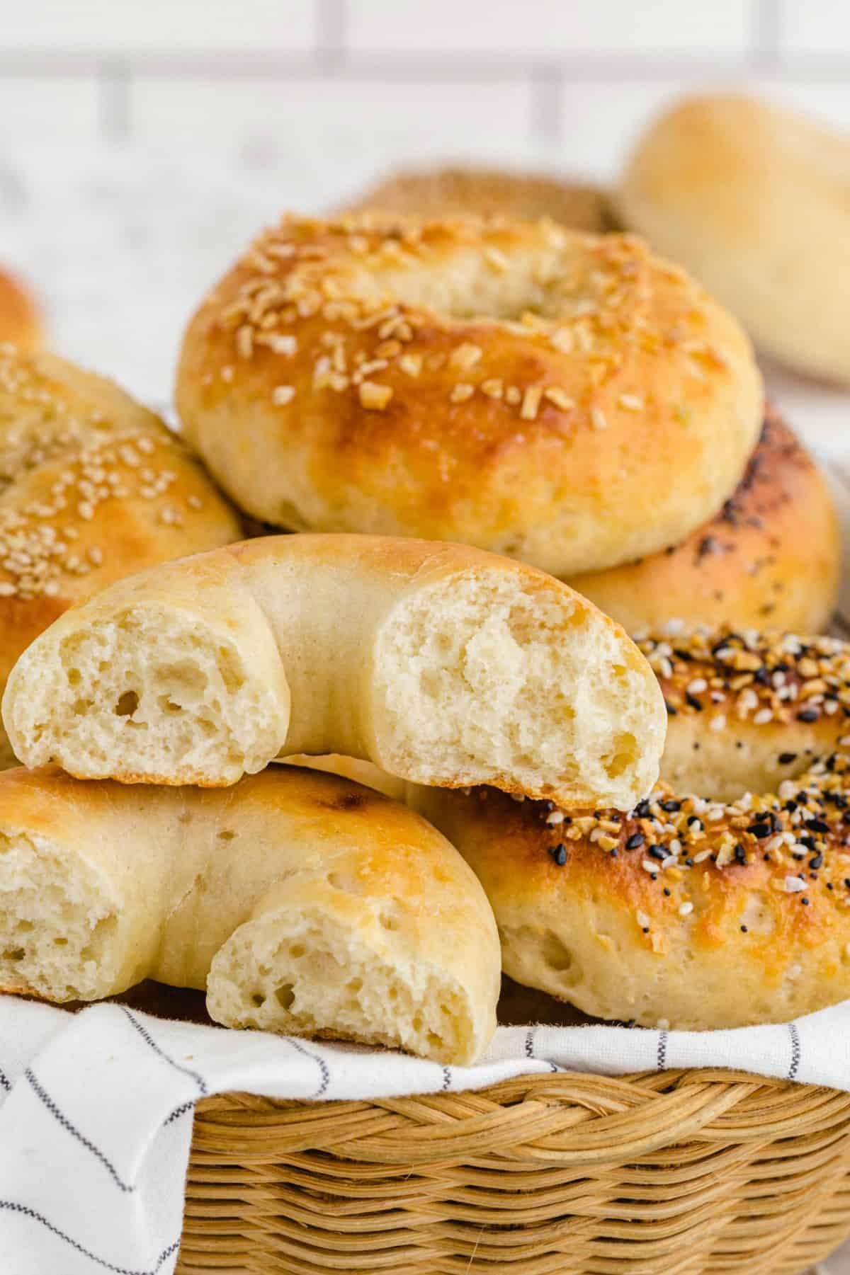 A basket of 2 Ingredient Bagels, with one bagel cut open, topped with various seasonings like sesame seeds and everything bagel mix.