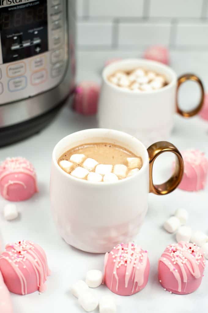 Pink Hot Chocolate Bombs around a cup of hot chocolate