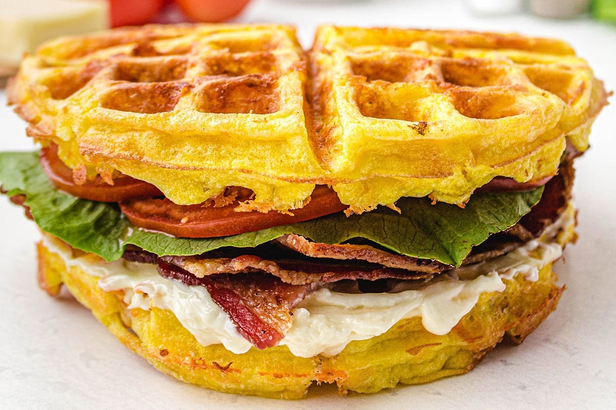 Two golden chaffles with sandwich with bacon, lettuce, and tomato.