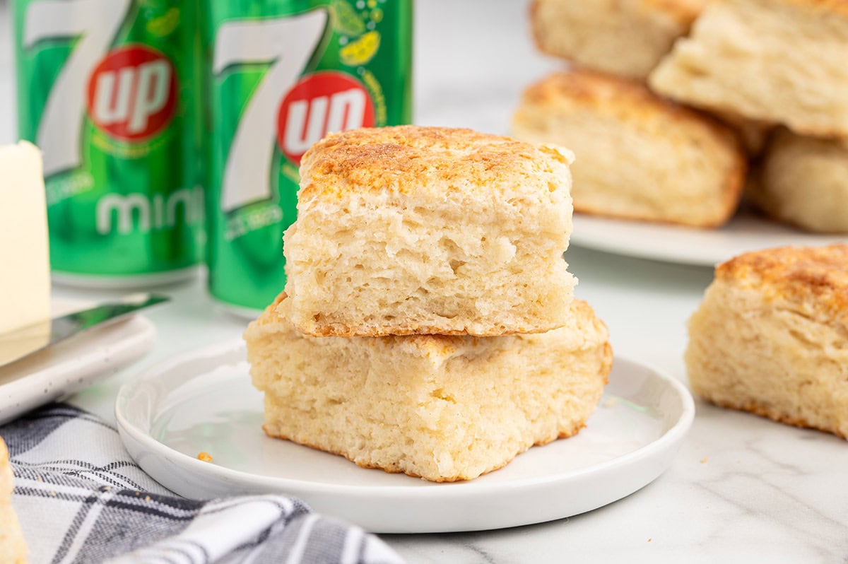 Two fluffy 7UP biscuits stacked on a plate with soda cans in the background.