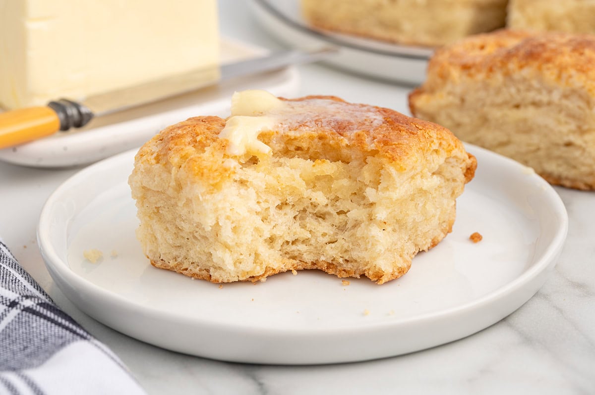 A 7UP biscuit with a bite taken out, topped with melted butter on a small plate.