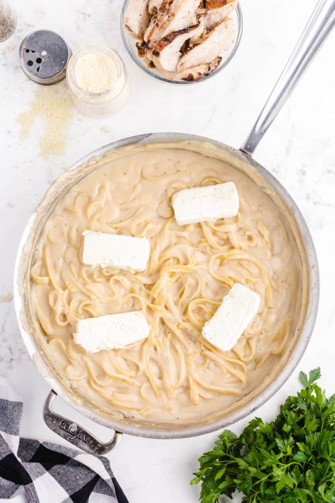 blocks of cream cheese added to a pot of cooked pasta