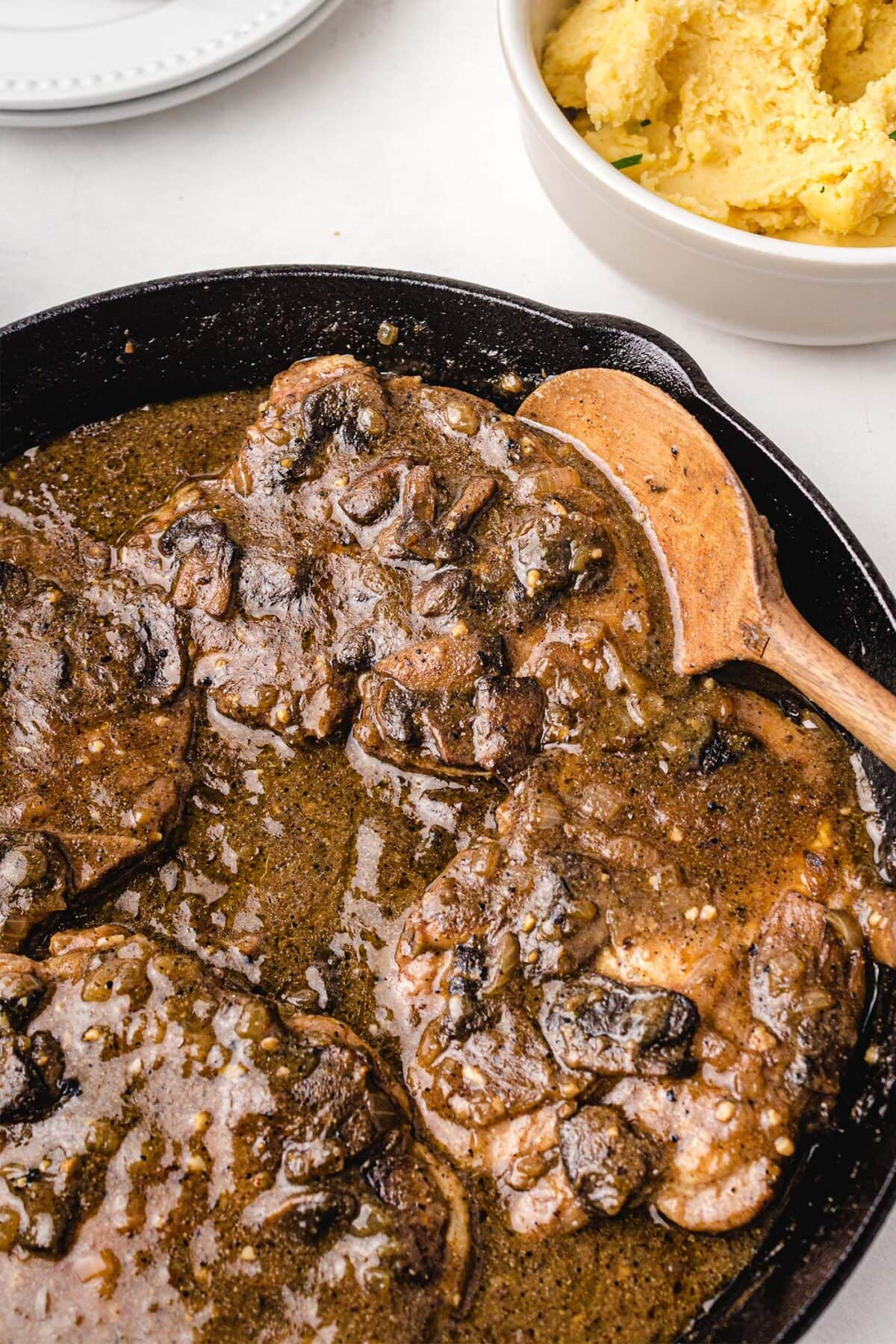 Smothered pork chops in a mushroom gravy sauce, served in a cast iron skillet.