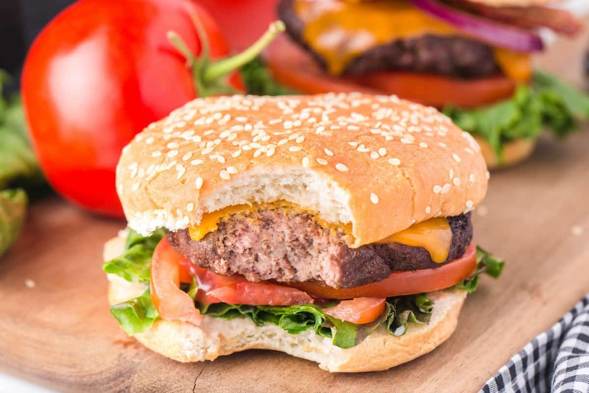 Juicy air fryer burger with a bite taken out, sesame bun, melted cheese, lettuce, tomato, and onion.