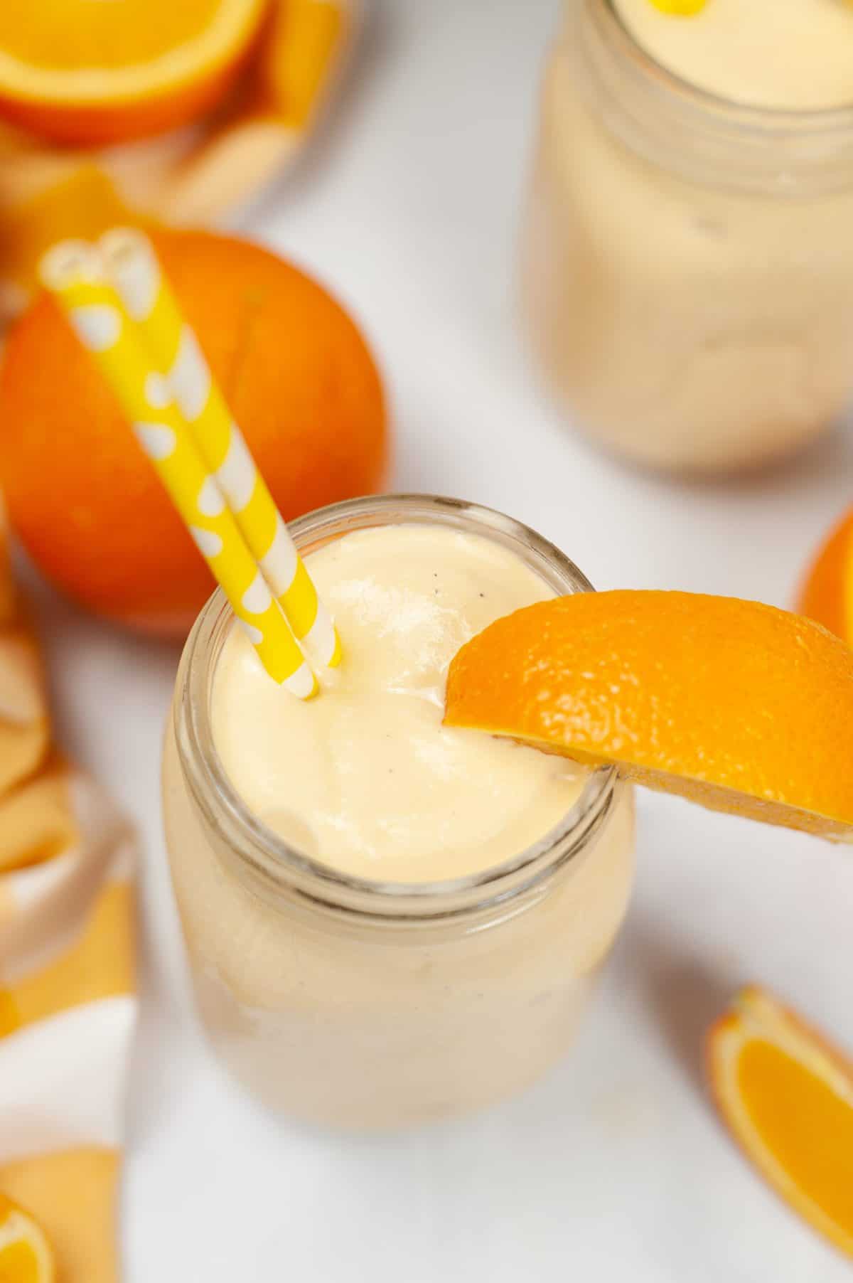 Close up of a creamy orange smoothie in a mason jar with an orange slice garnish and striped paper straws.