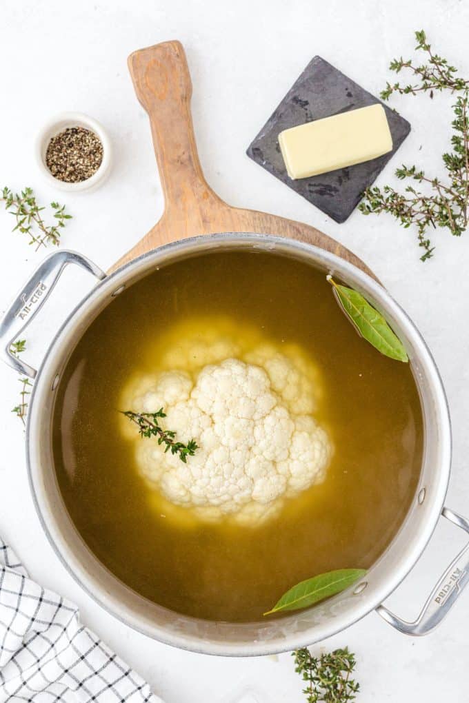 cauliflower in a stock pot with broth, bay leaves, and thyme.