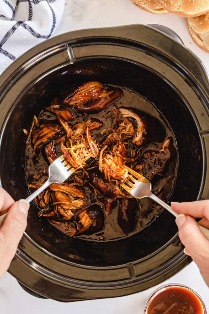 shredding chicken with fork and mixing with sauce