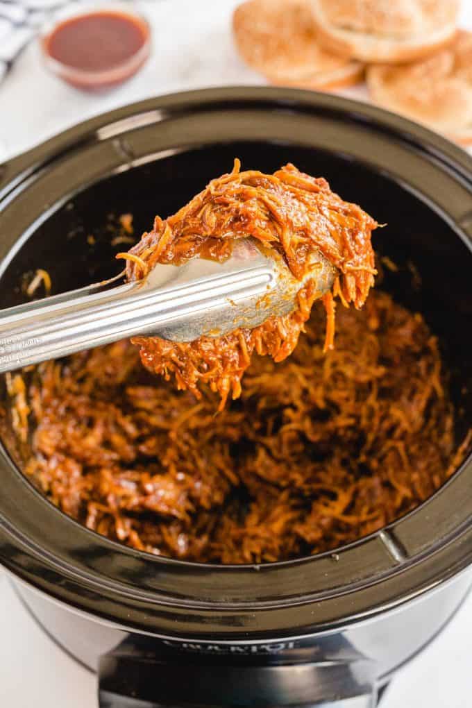 picking up a portion of pulled chicken with tongs