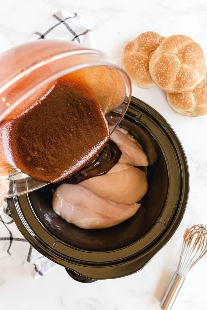 pouring sauce into the chicken inside slow cooker