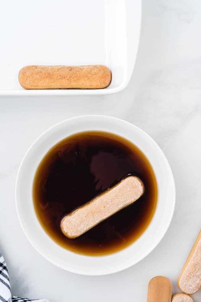 Dipping both sides of the lady fingers in the coffee mixture.