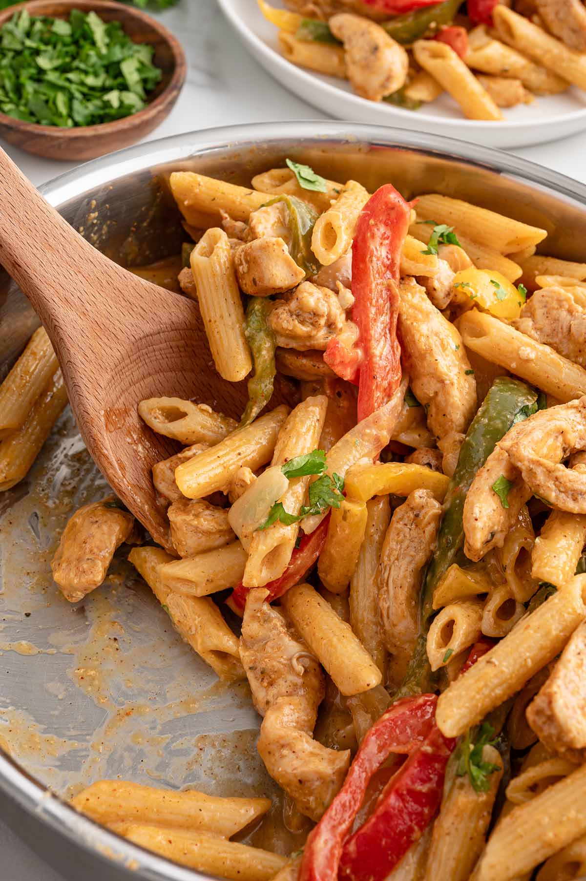 chicken fajita pasta in skillet with a wooden spoon.