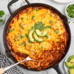 enchilada skillet on the table garnished with fresh cilantro and avocado slices.