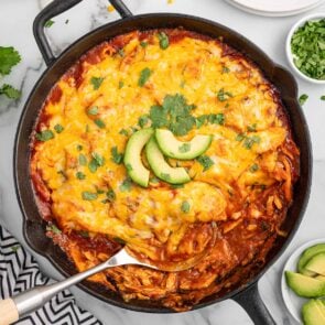 enchilada skillet on the table garnished with fresh cilantro and avocado slices.