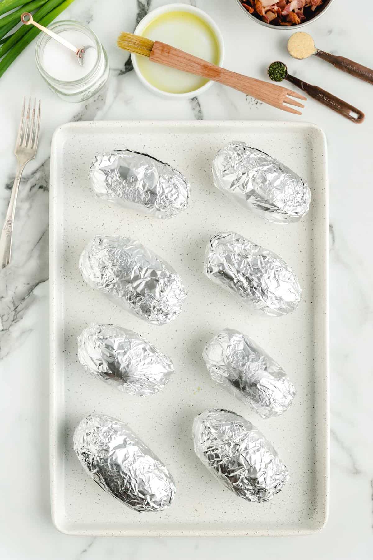 potatoes wrapped in foil on top of baking sheet