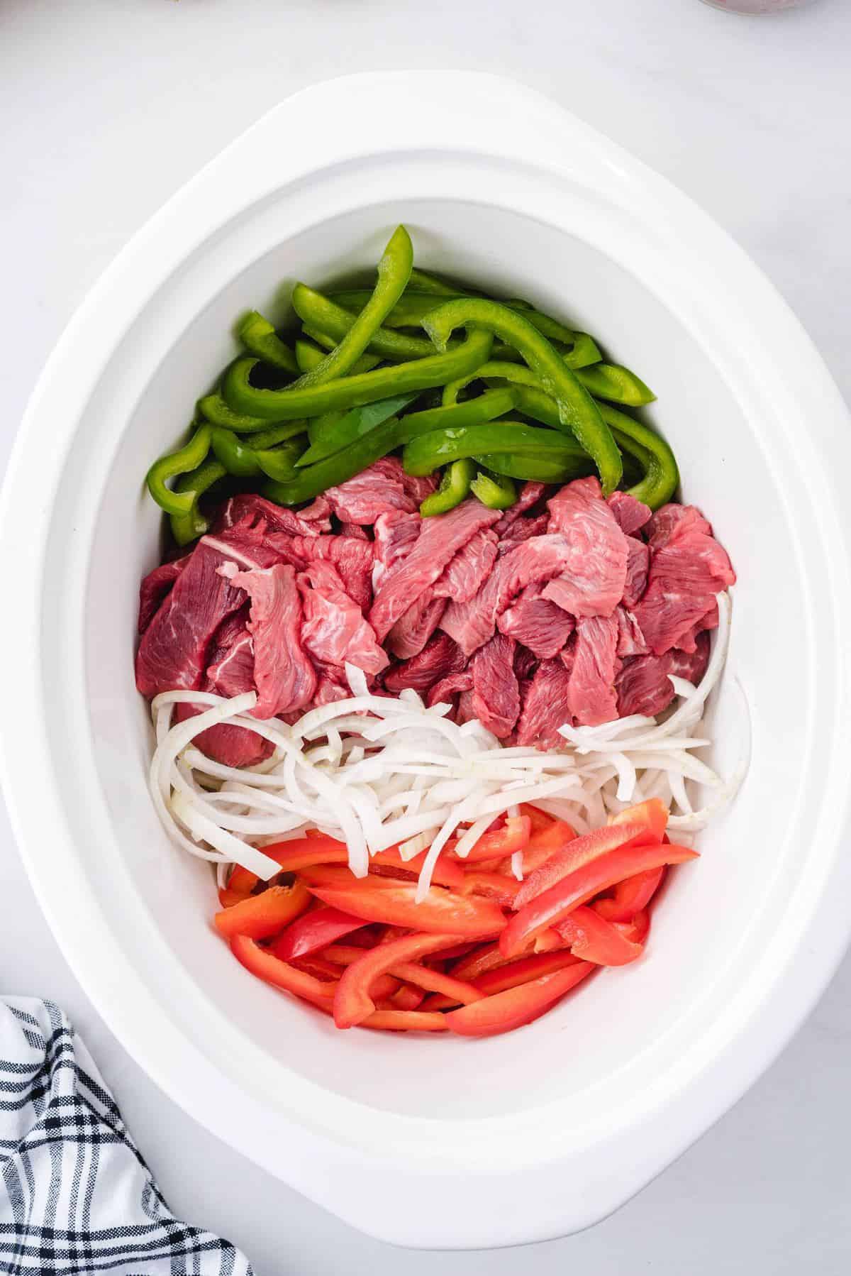 Add beef strips, red and green peppers, and onions to the Crockpot.
